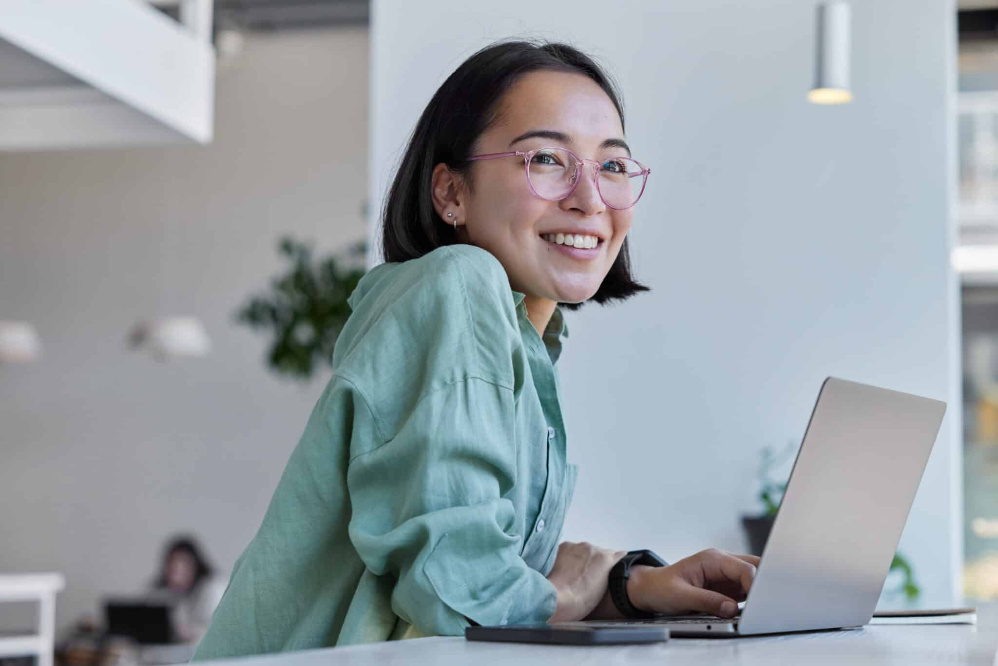 Student sits in front of open laptop and smiles to the camera.