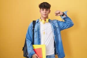 Teenager wearing denim shirt and white t-shirt with a backpack and headphones carrying school books. Yellow background. 